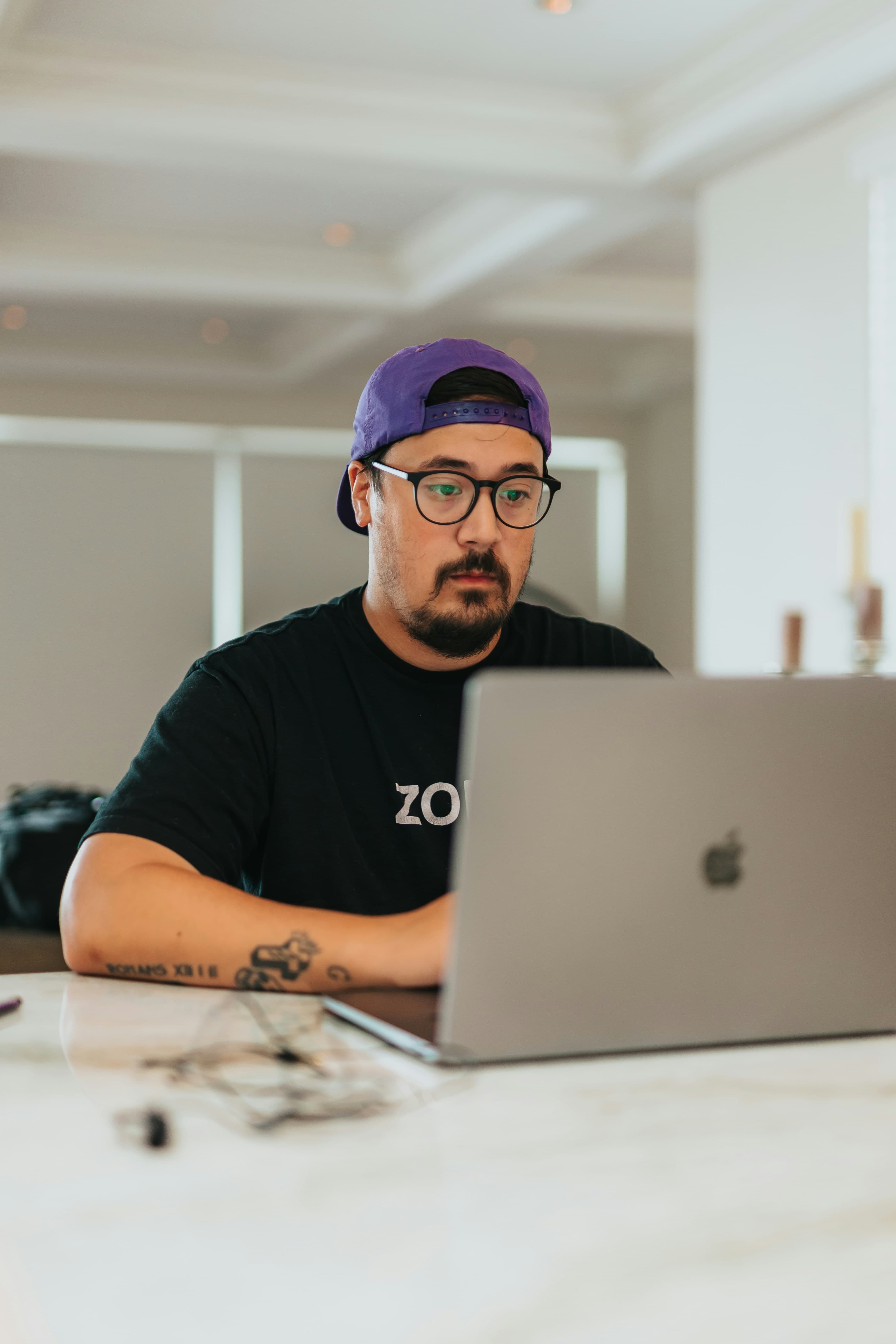 Entwickler mit Basecap arbeitet konzentriert an einem Laptop an einem hellen Tisch
